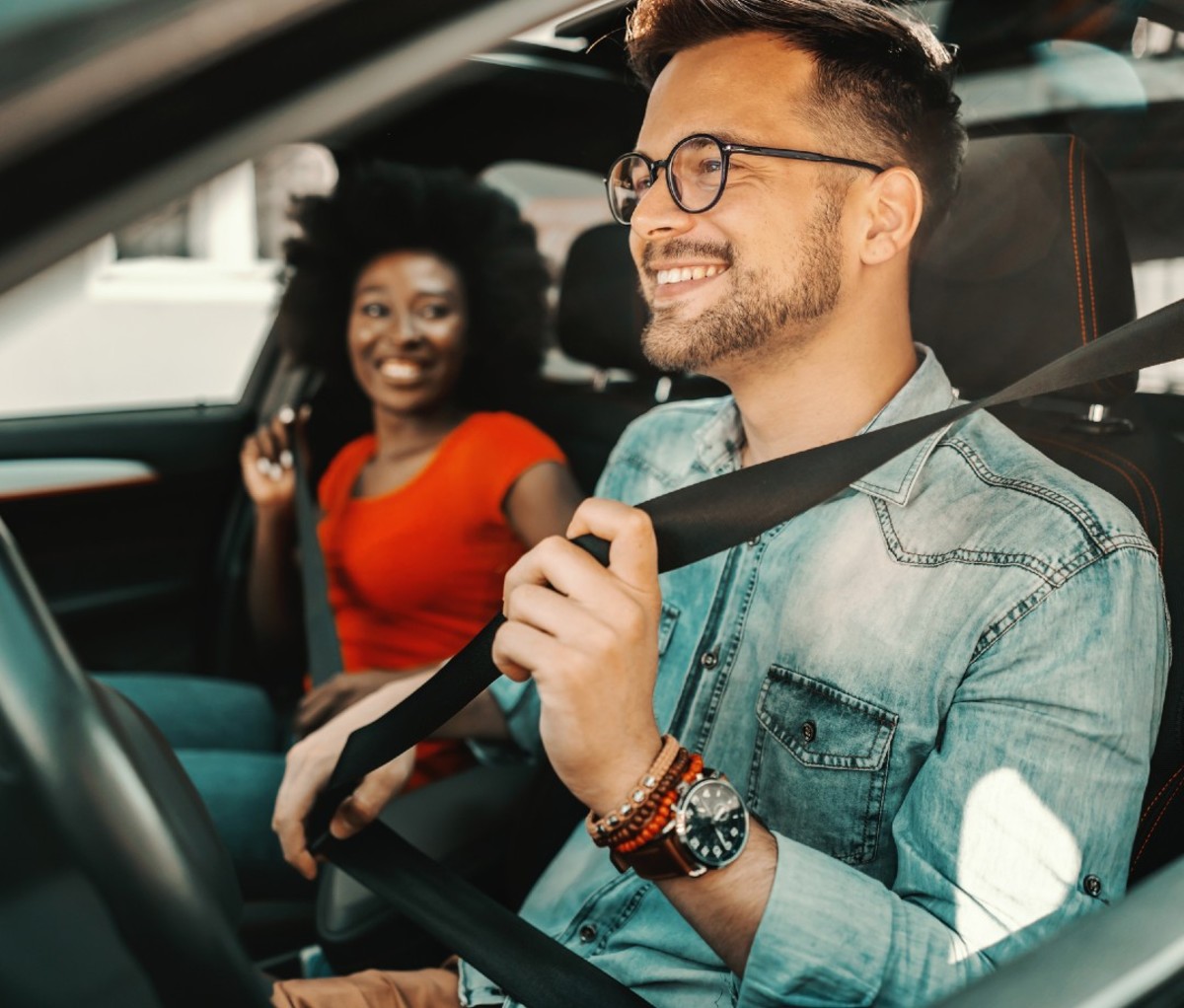 Caucasian man buckling seat belt next to Black woman in car
