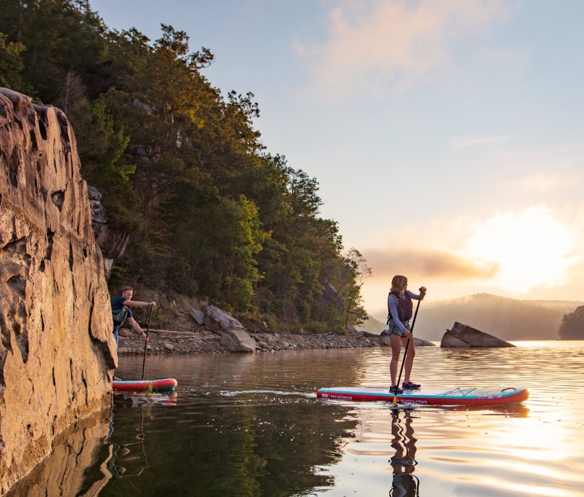 Man and woman standup paddle boarding on lake at sunset