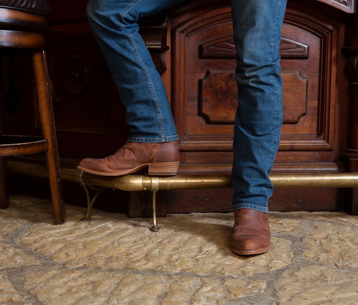 Men's legs in denim and brown boots standing against bar