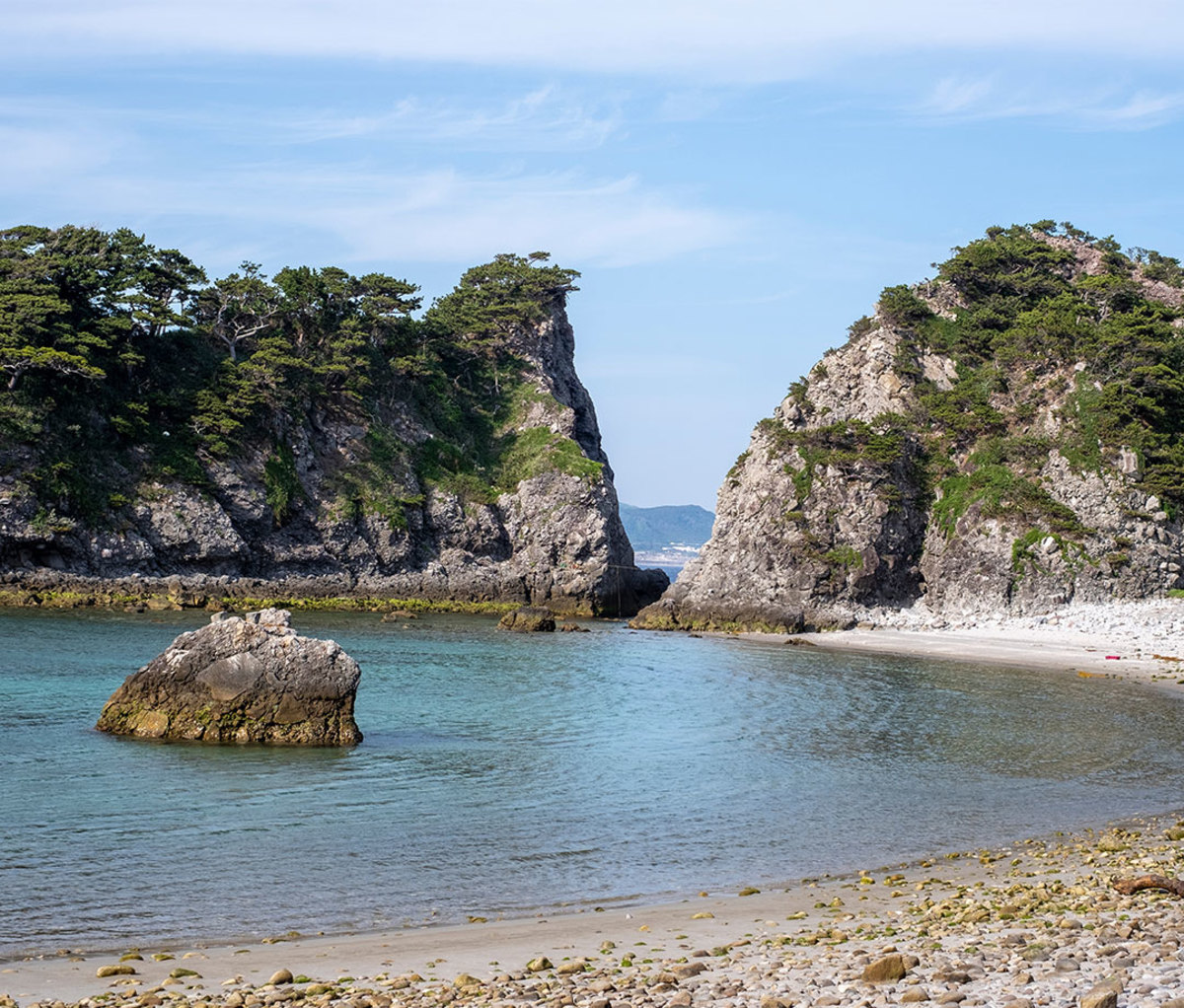View of the marine blue ocean at the deserted Tomari Beach enclosed by steep rocky cliffs
