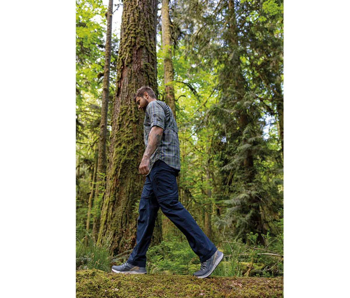 Man wearing flannel shirt and blue pants walking through woods