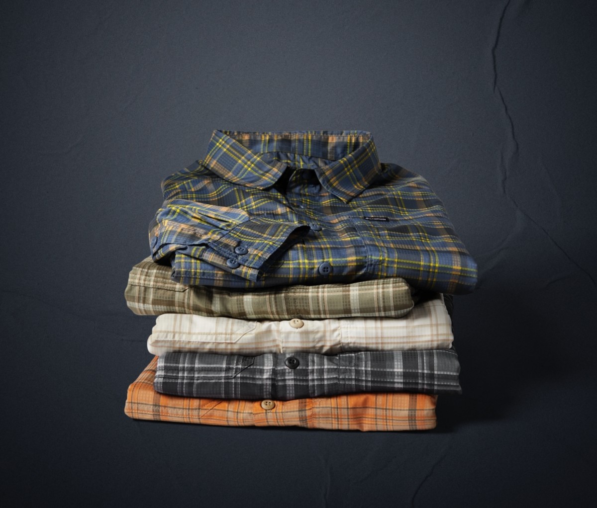 Stacked pile of folded Columbia Silver Ridge Shirts on a grey background