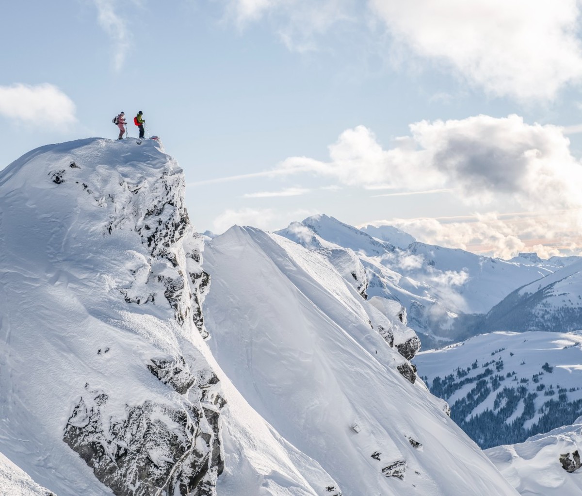 Two skiers standing on top of ski dropoff
