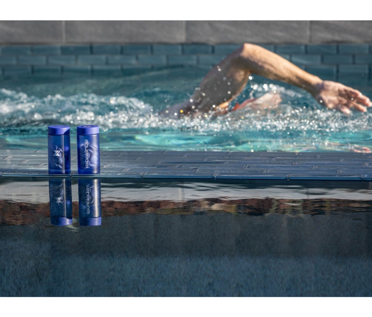 Man swimming laps in pool with blue supplement bottles in foreground