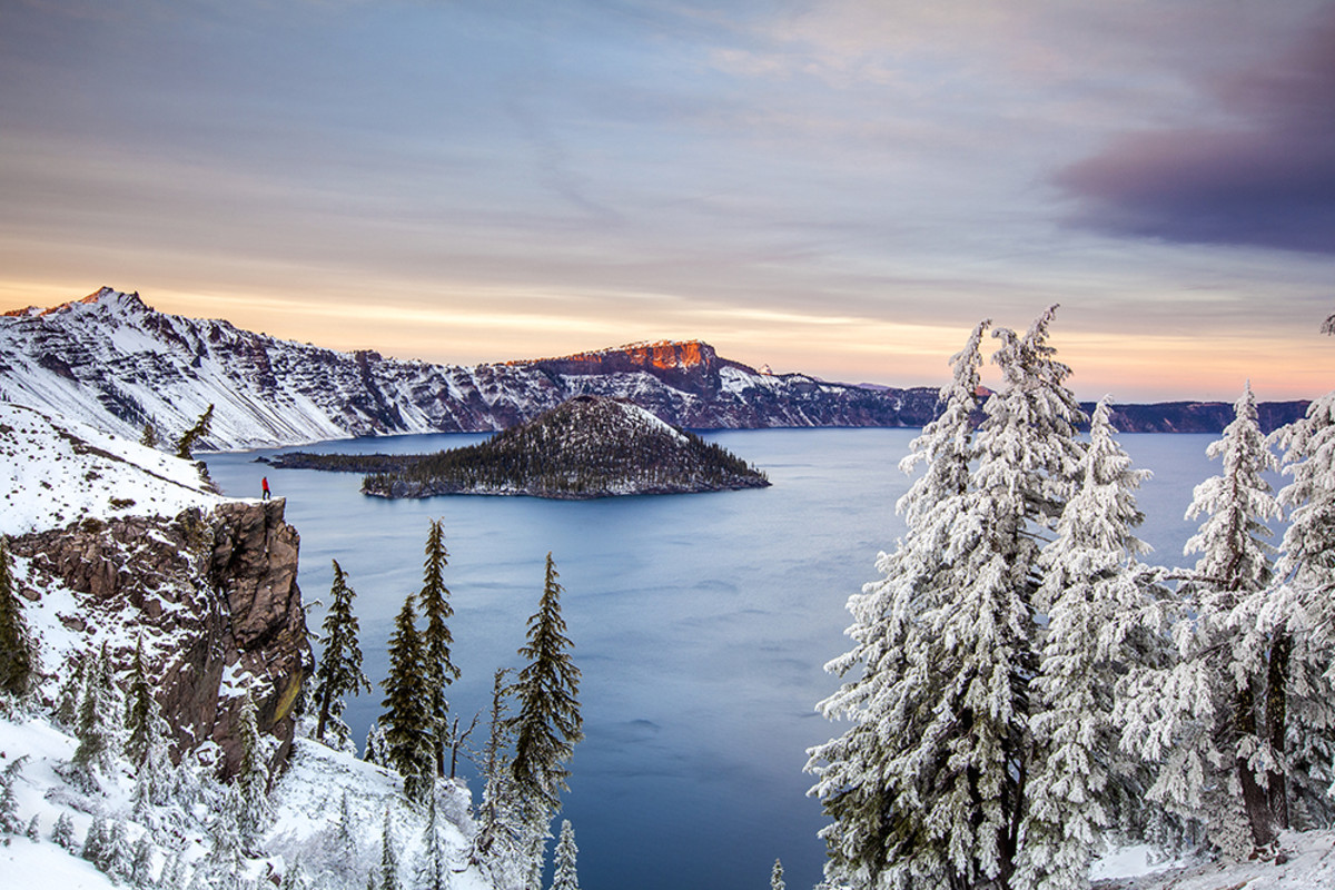 Crater Lake National Park, Oregon: A man stands on a cliff overlooking Crater Lake in early winter at sunset.