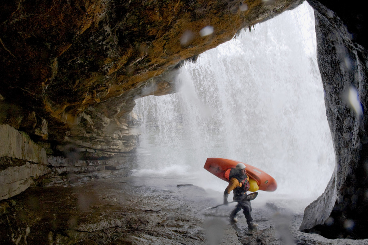 Attractive male kayaker standing underneath a waterfall.