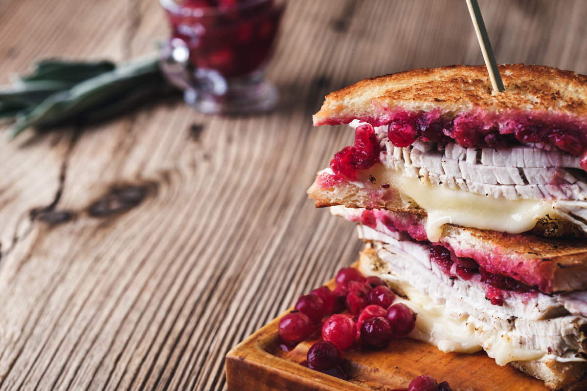 Thanksgiving turkey sandwich with brie cheese and cranberry sauce on cutting board.