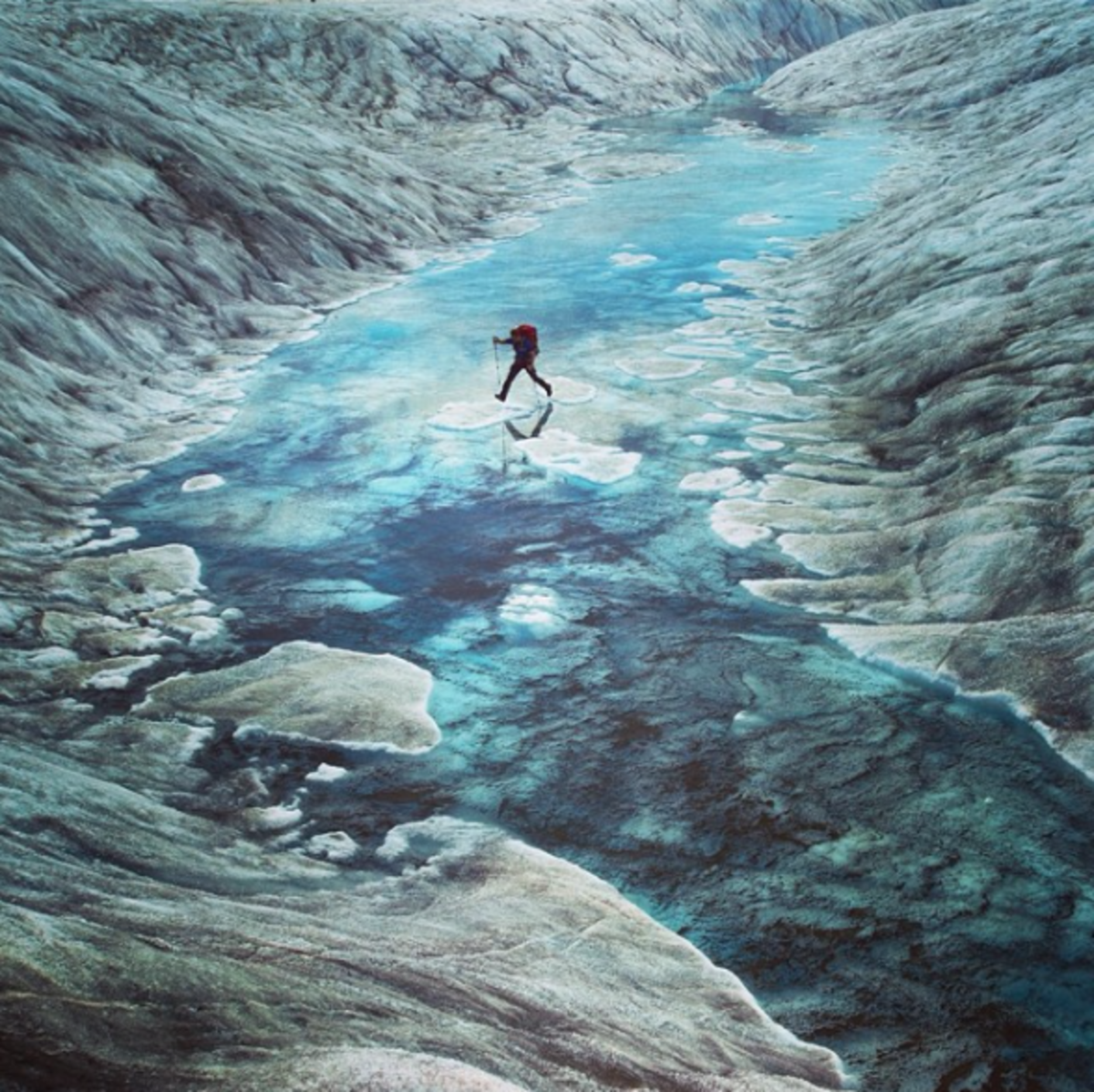 A climber jumps between islands of ice in a shallow glacial pool on Ruth Glacier. Photo by Aaron Huey from Facebook and Instagram