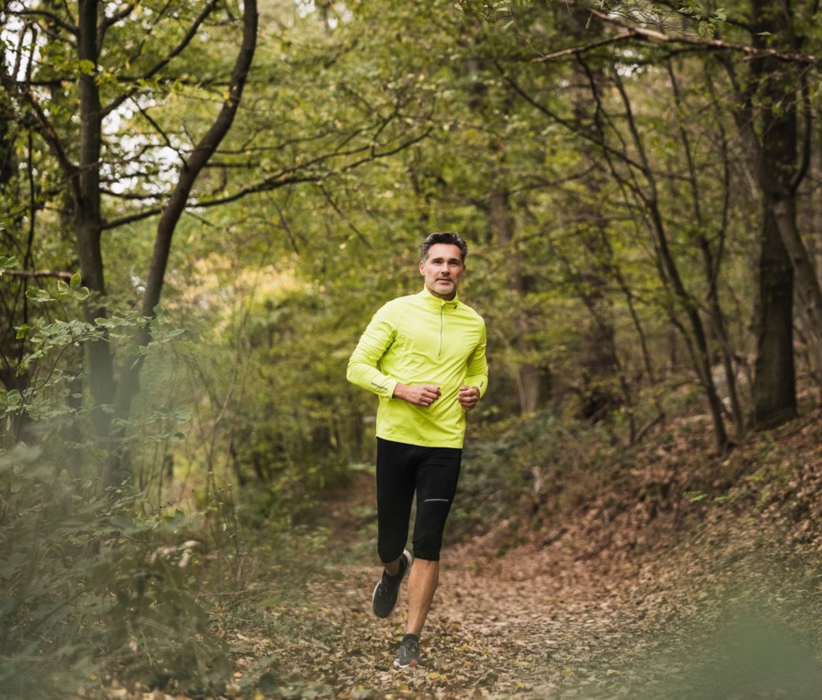 Man in a yellow shirt running through a forest. running benefits