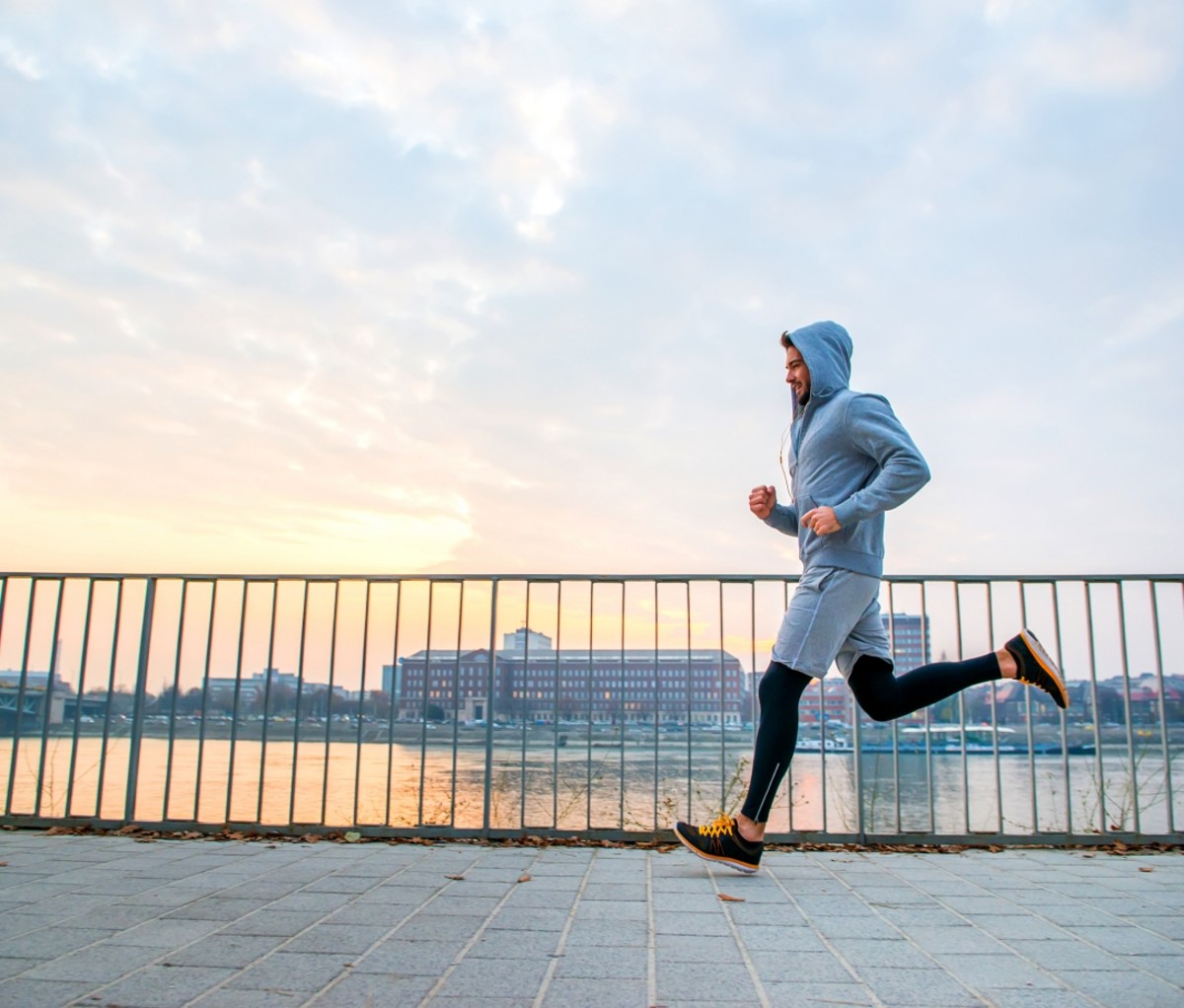 Man in a grey hoodie running along a river. running benefits