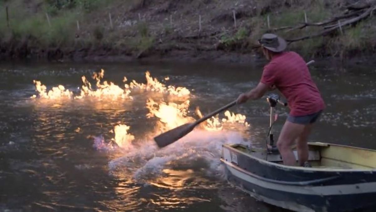 The Condamine River was set on fire by an Australian politician to make a statement. Here a man uses a paddle in an attempt to extinguish the flames.