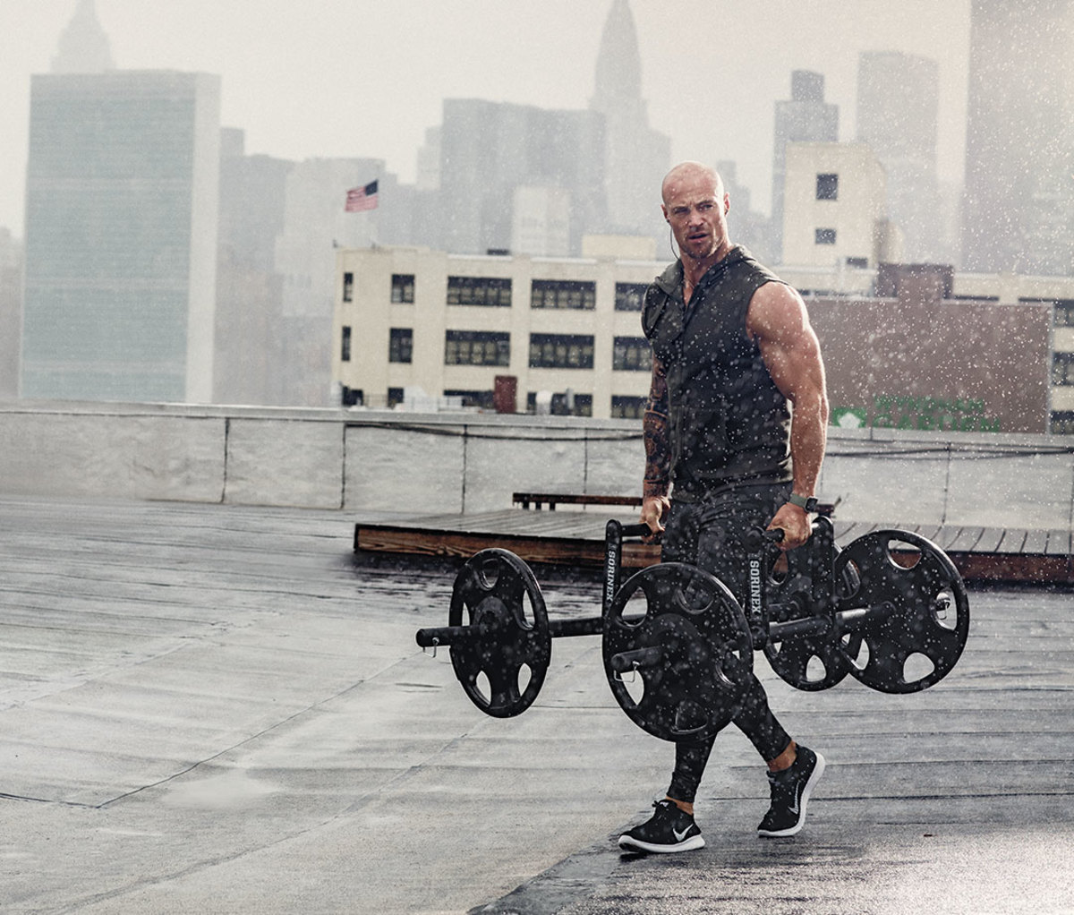 Man doing farmer's carry with hex bar deadlift on rooftop in the rain