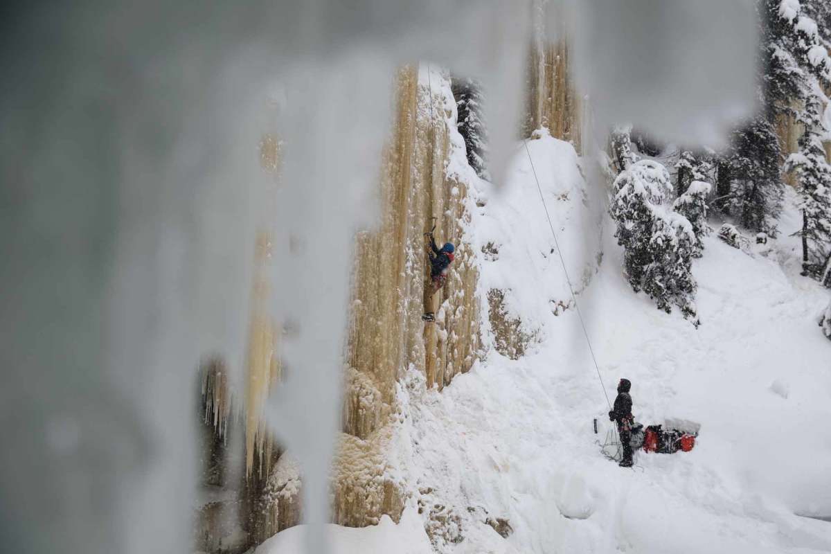 A view through ice of two men ice climbing on a frozen waterfall in Tumbler Ridge.