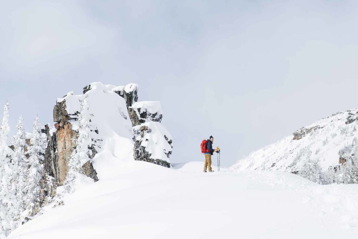A man standing next to a rock formation in the snow on a hike in Tumbler Ridge.