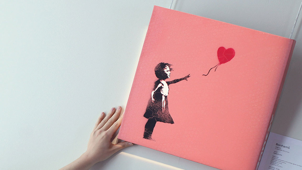 A Bonhams intern poses with a work by Banksy entitled 'Balloon Girl', at Bonhams Auction house on September 16, 2011 in London, England. The piece makes up part of the 'Urban Art' sale which takes place on September 21, 2001 at Bonhams Auction house in London. (Photo by Dan Kitwood/Getty Images)
