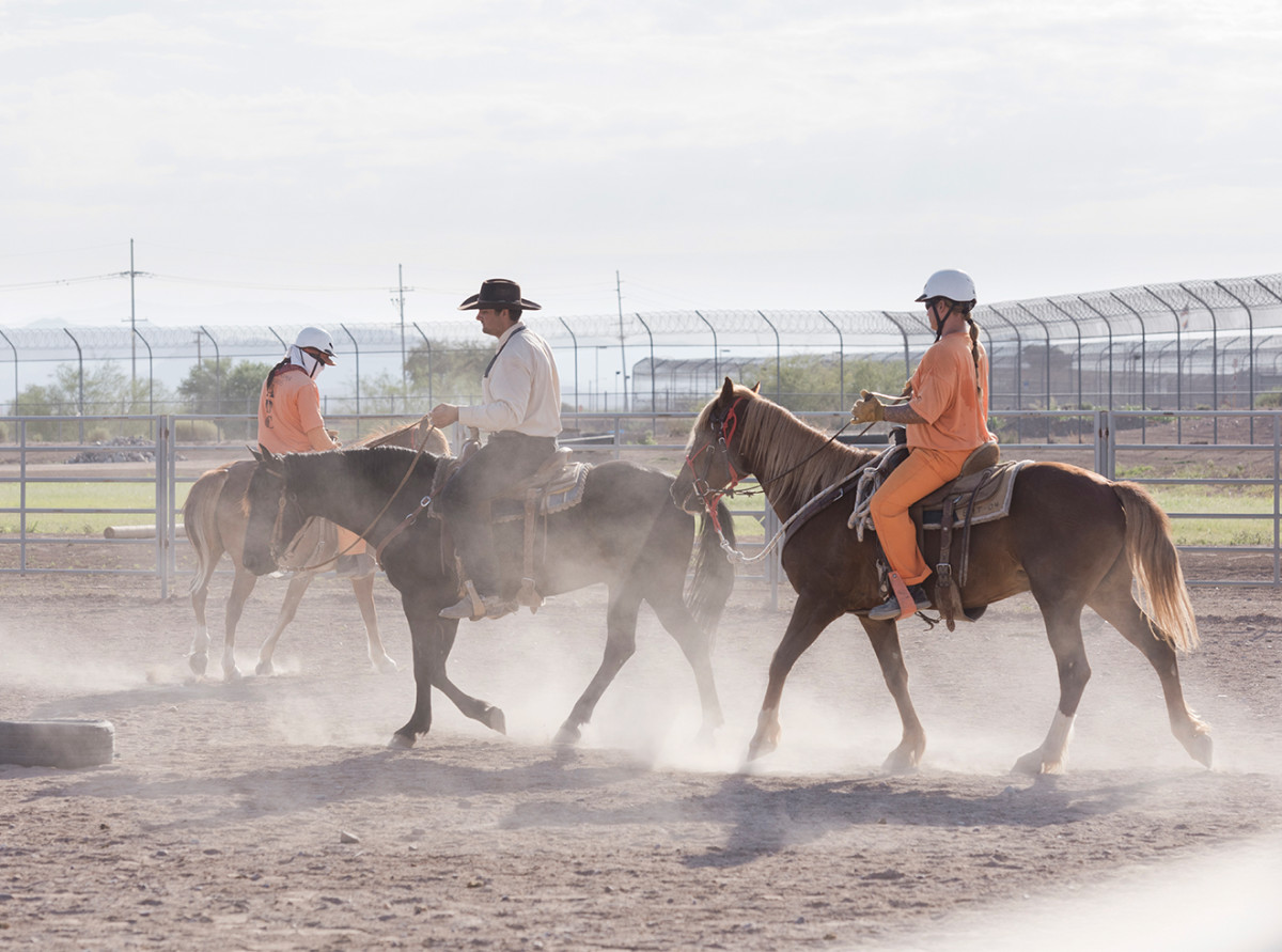 Two inmates ride in a prison corral.