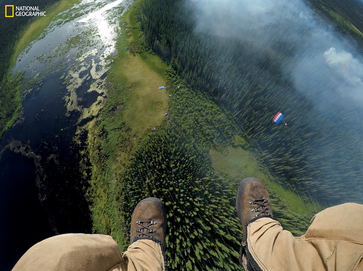 Matt Oakleaf, camera mounted on his gear bag, drops behind the rest of his team to a landing site near smoldering boreal forest. Jumpers can put on 100 pounds of gear and get on a plane in minutes. Their mission: extinguish fires before they rage out of control. (Photograph by Mark Thiessen / National Geographic)