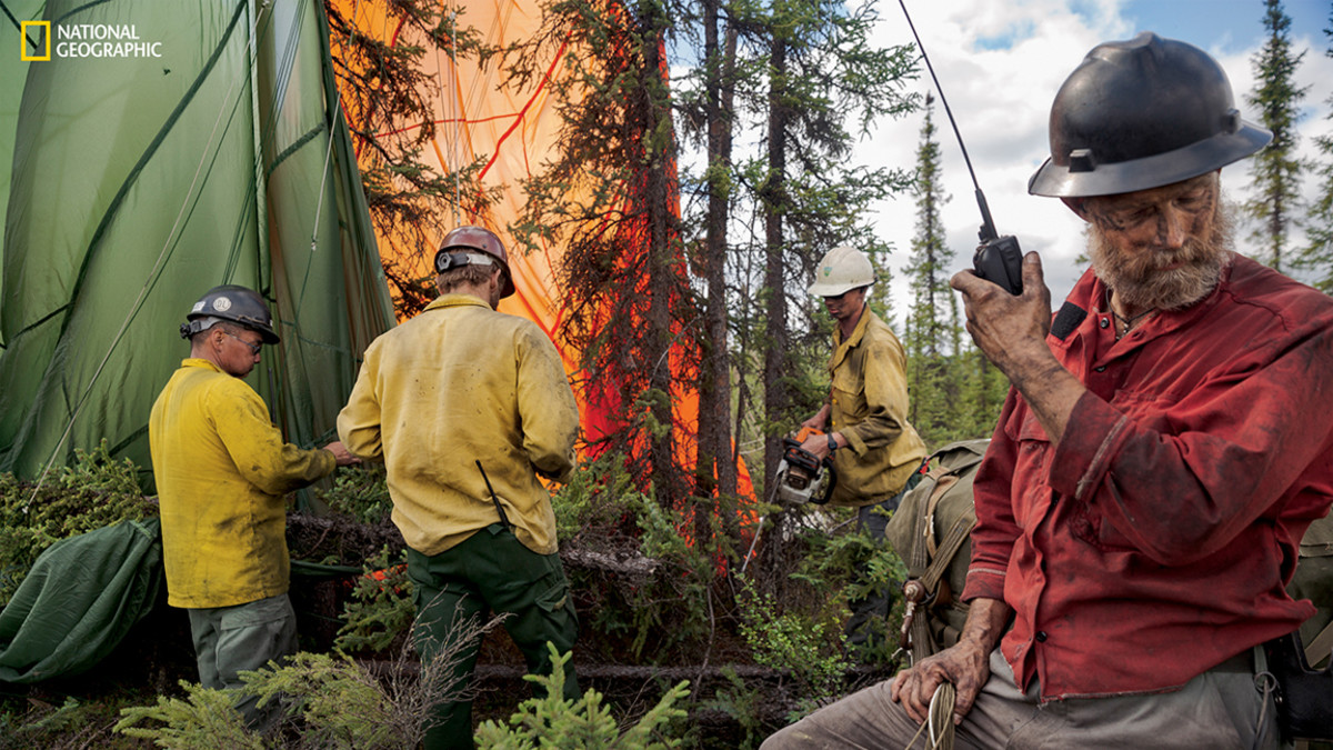 Incident commander Ty Humphrey communicates with a pilot who has dropped a pallet of cargo near a fire. Crew members free the chute from the tree where the load landed. (Photograph by Mark Thiessen / National Geographic)