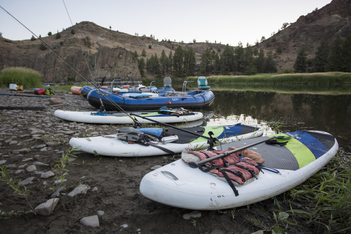 SUPs and rafts wait on the edge of a river.