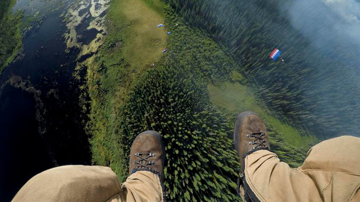 Matt Oakleaf, camera mounted on his gear bag, drops behind the rest of his team to a landing site near smoldering boreal forest. Jumpers can put on 100 pounds of gear and get on a plane in minutes. Their mission: extinguish fires before they rage out of control. (Photograph by Mark Thiessen / National Geographic)