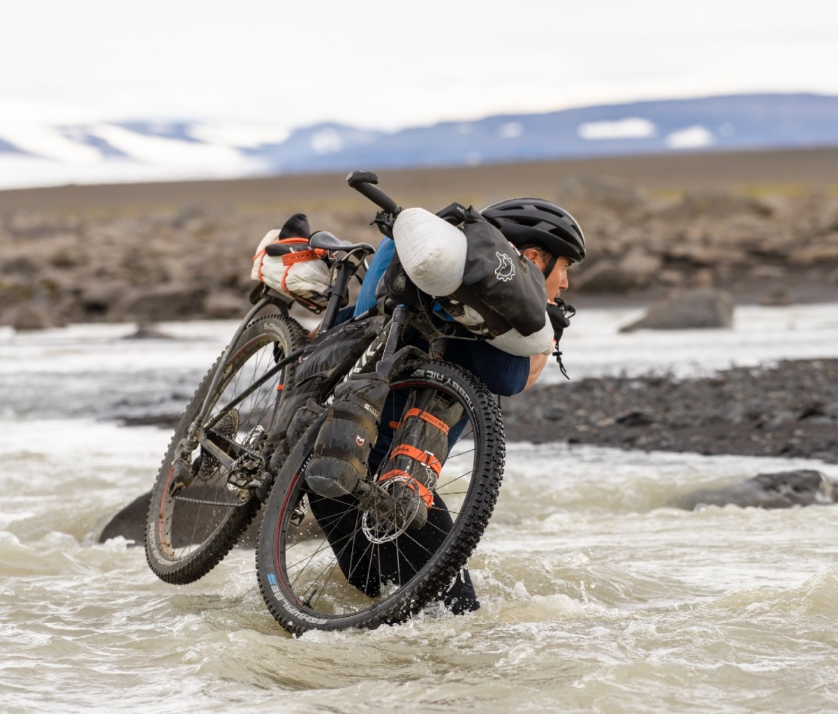 Chris Burkard carrying his bike and gear across a river.