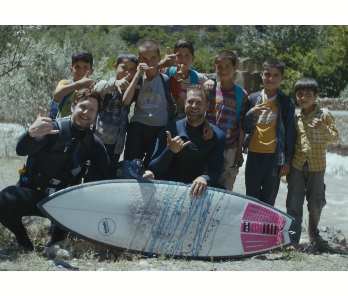 Jacob Kelly Quinlan poses with local kids after surfing a river in Afghanistan