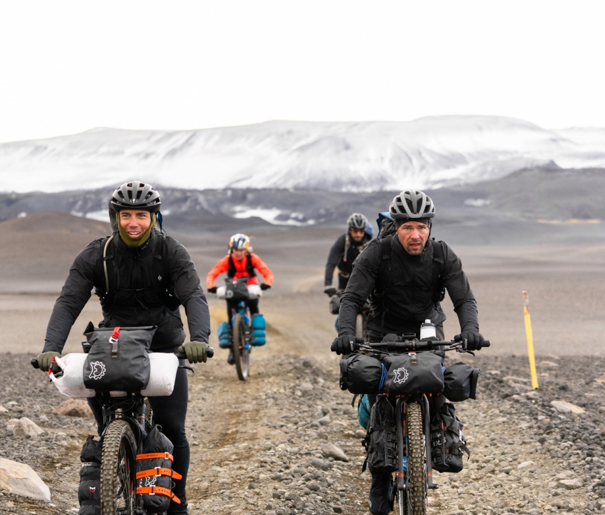 Chris Burkard, Emily Batty, Adam Morka, And Eric Batty Biking With Glaciers In The Background.