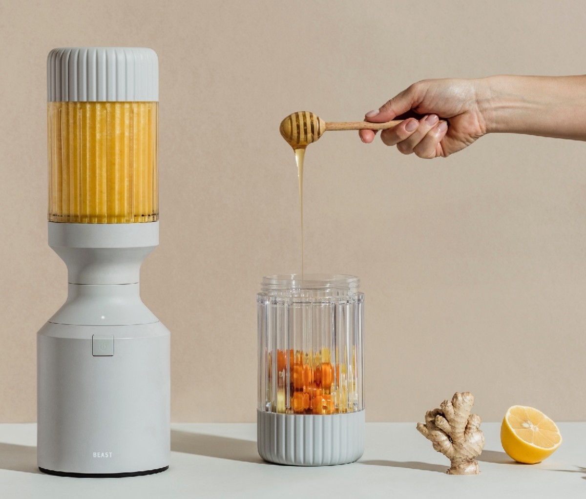 Someone pours honey into a Beast B10 + Health mixer with carrots, lemon, and ginger