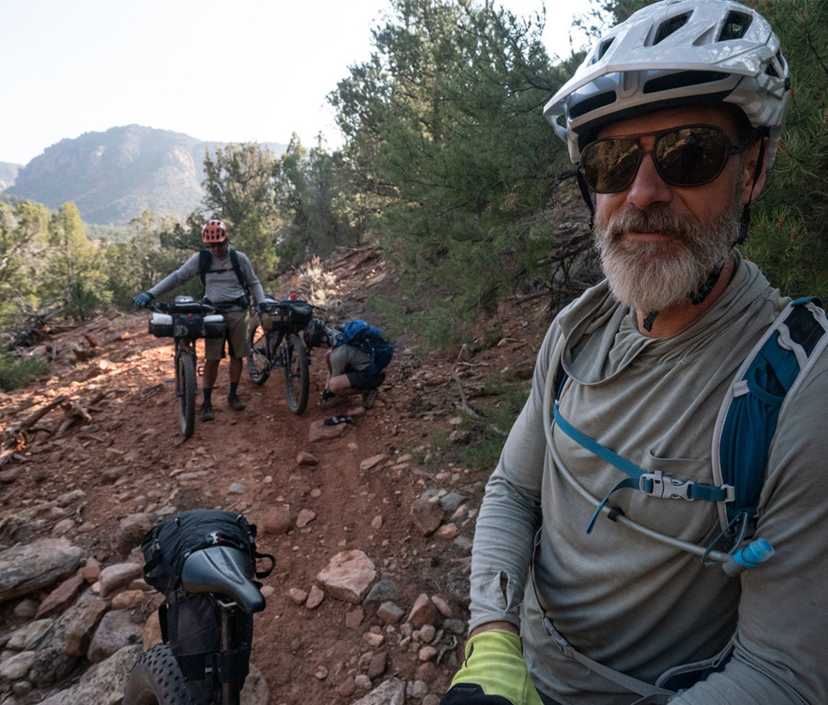 Male mountain bikers pause to catch their breath and make bike adjustmets in desert landscape.