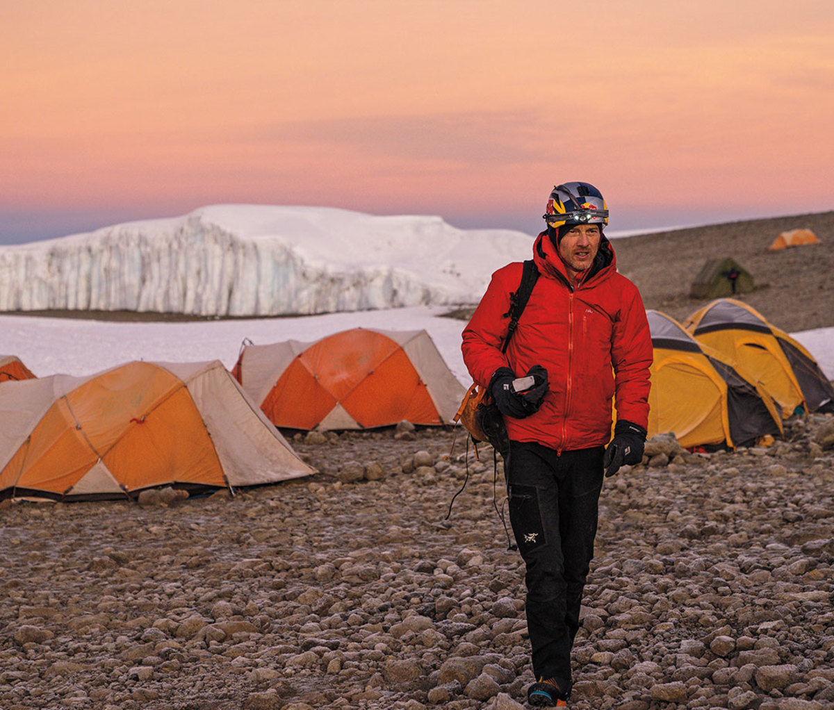 Will Gadd walking way from orange tents with iceberg in the distance