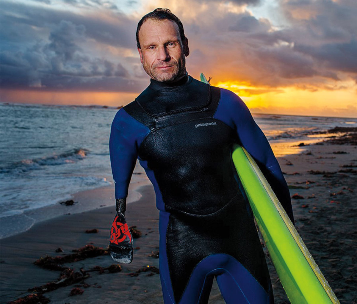 Portrait of Jeff Denholm holding surfboard against a sunset