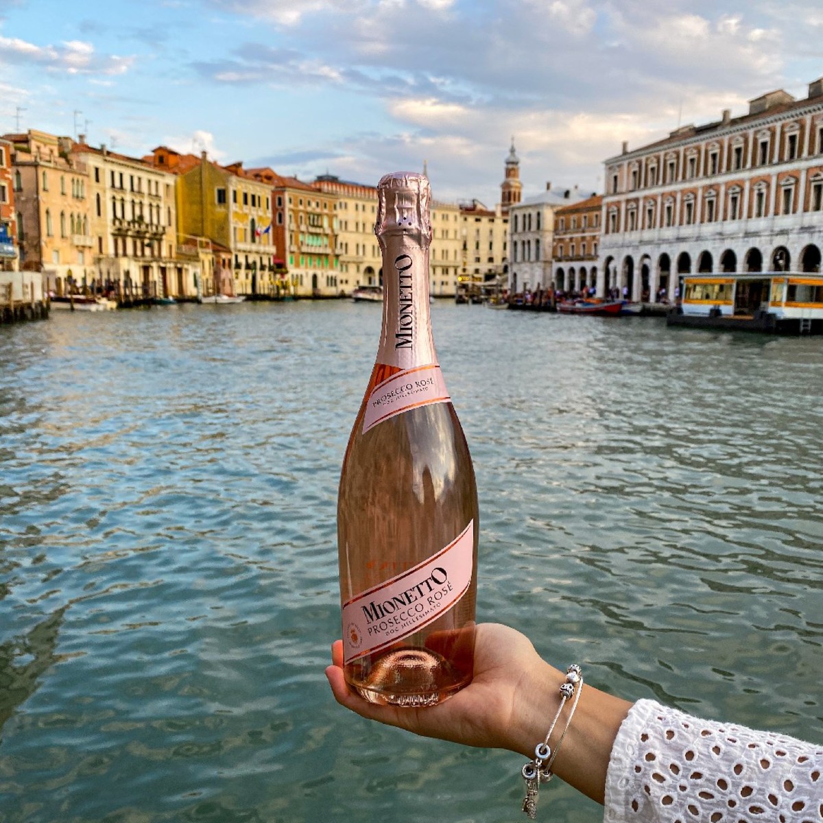 Woman holding bottle of Mionetto Prosecco Rosé DOC in front of canal in Venice