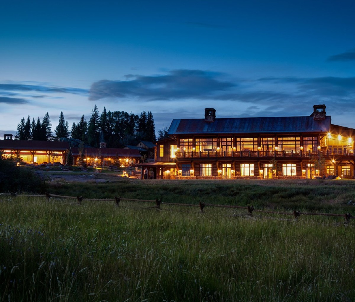 Een nachtelijk uitzicht op The Lodge & Spa op Brush Creek Ranch. Hoog gras is op de voorgrond, de lichten zijn allemaal aan in de Lodge.