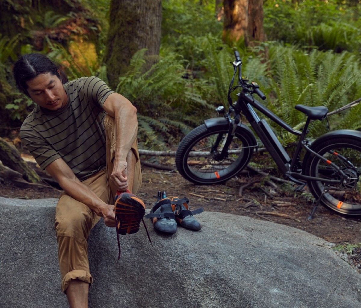 Climber putting rock climbing shoes on with electric fat bike behind him
