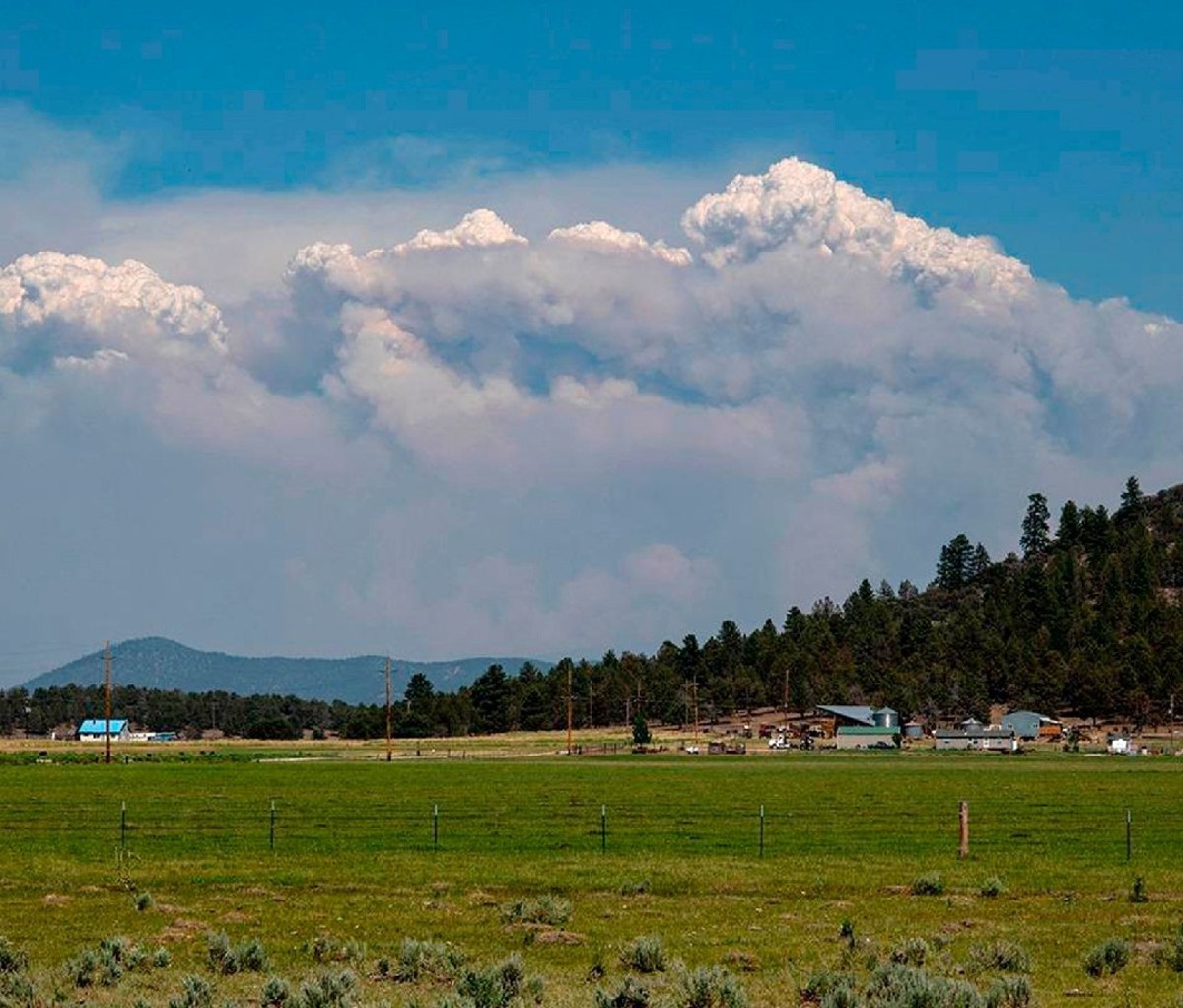 Tall plumes of smoke from the Bootleg Fire forms on the horizon of southern Oregon farmland.