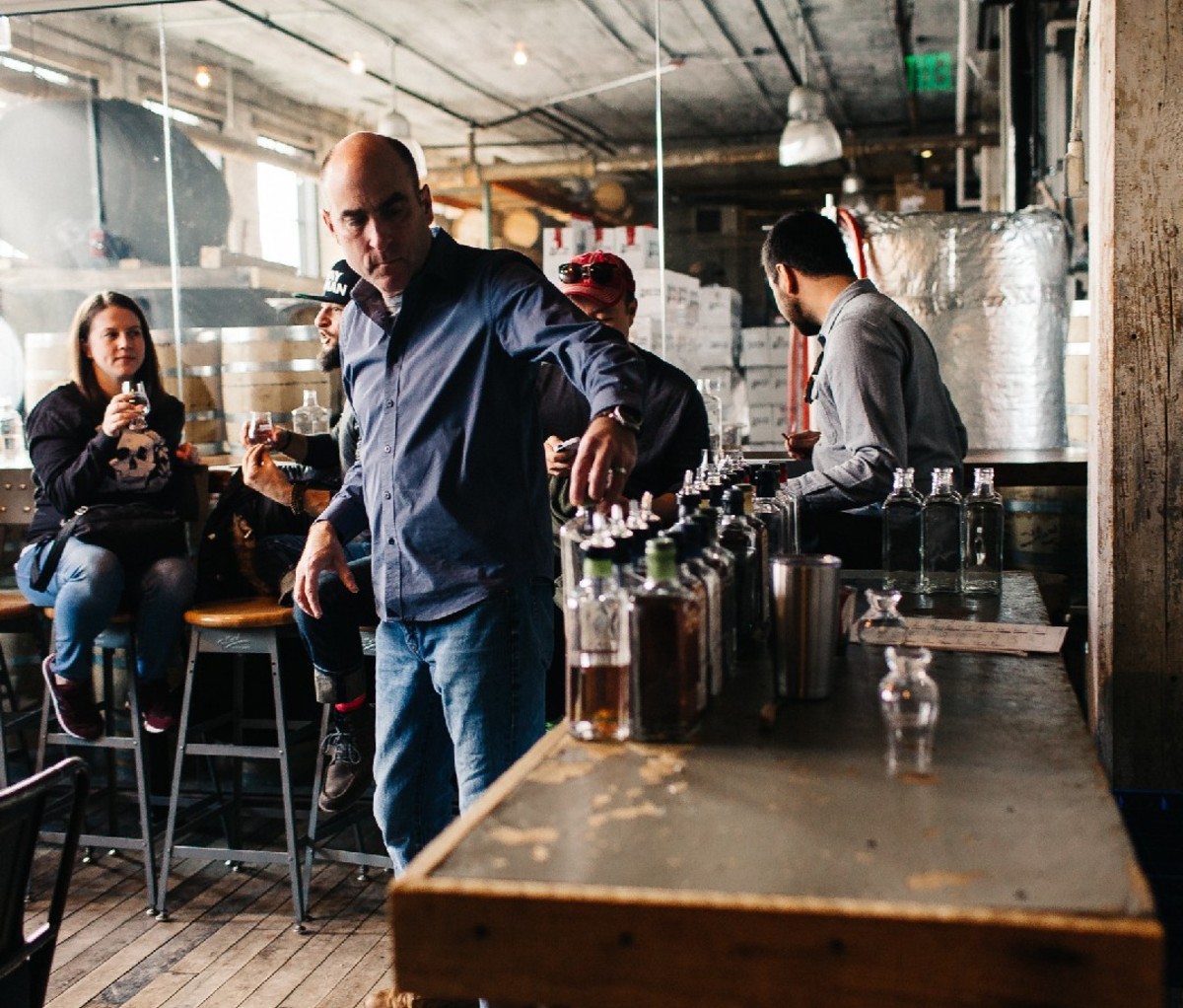 Patrons proeven sterke drank en een man kijkt naar een rij flessen bij Journeyman Distillery in Three Oaks, Michigan.