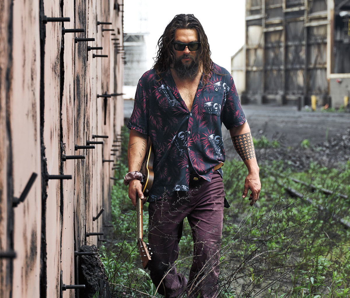 Jason Momoa walking through field with guitar in hand