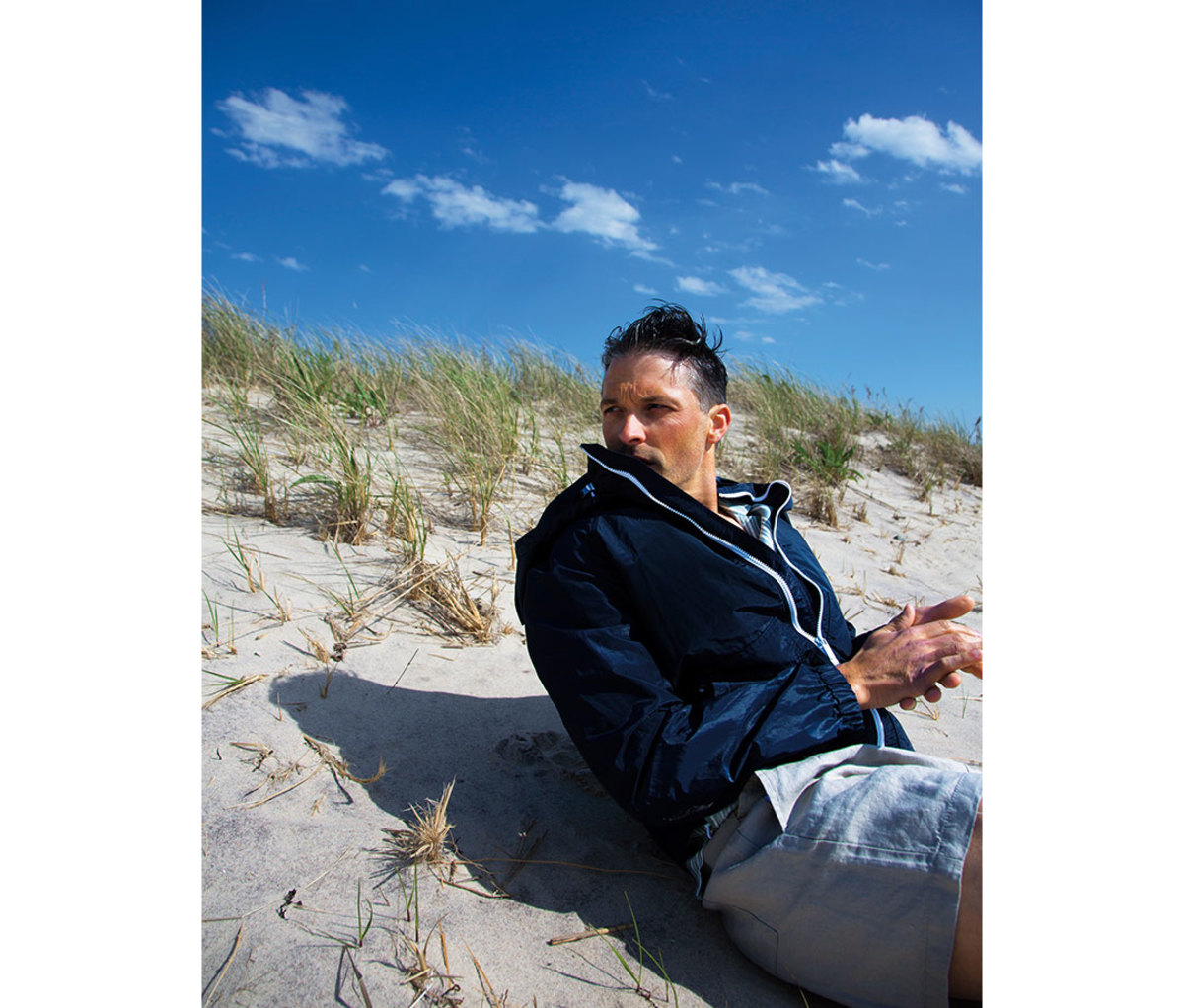 Man sitting on beach wearing blue hoodie and shorts