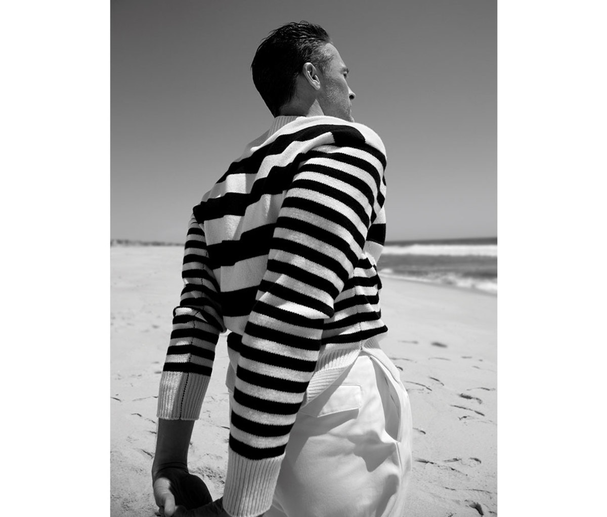 Black and white photo of man wearing striped sweater on beach