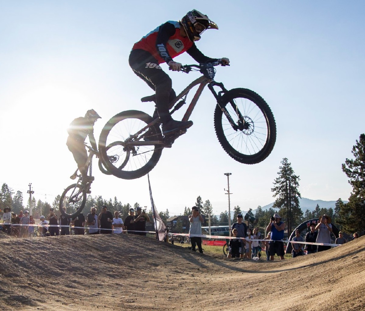 Two bike racers jump high above the course.