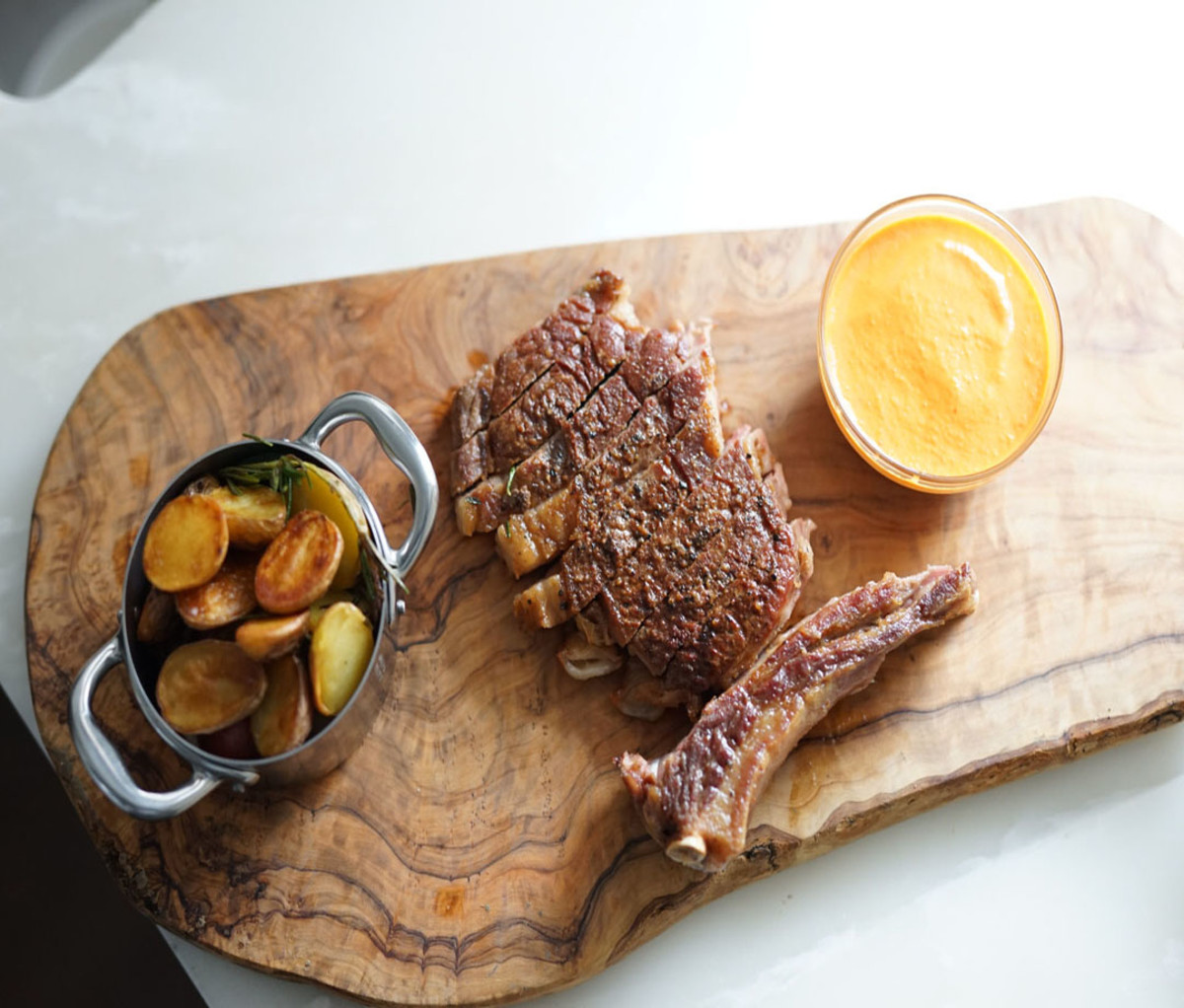 Ribeye laid out on a wooden platter with a dipping sauce and side dish