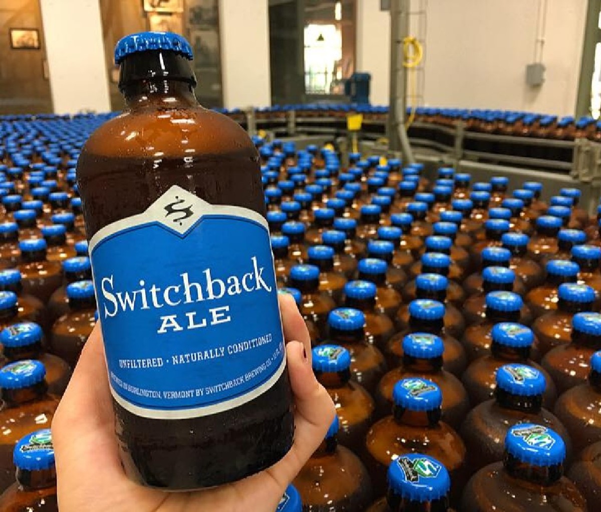A bottle of Switchback Brewing Co. Switchback Ale in front of a bottling line featuring many more beers.