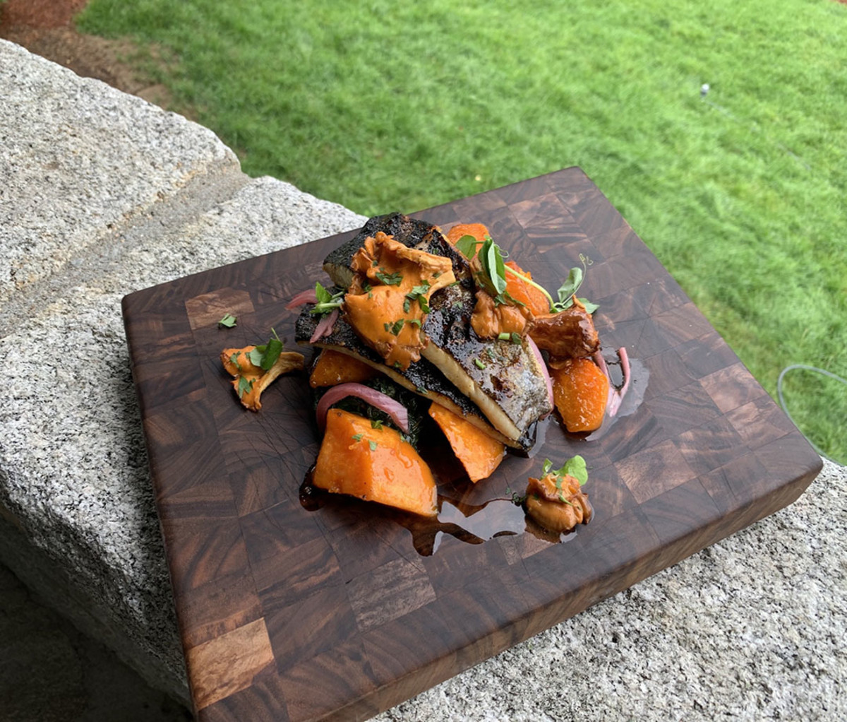 Grilled Trout with Sweet Potatoes and Braised Greens on a platter sitting on a wall