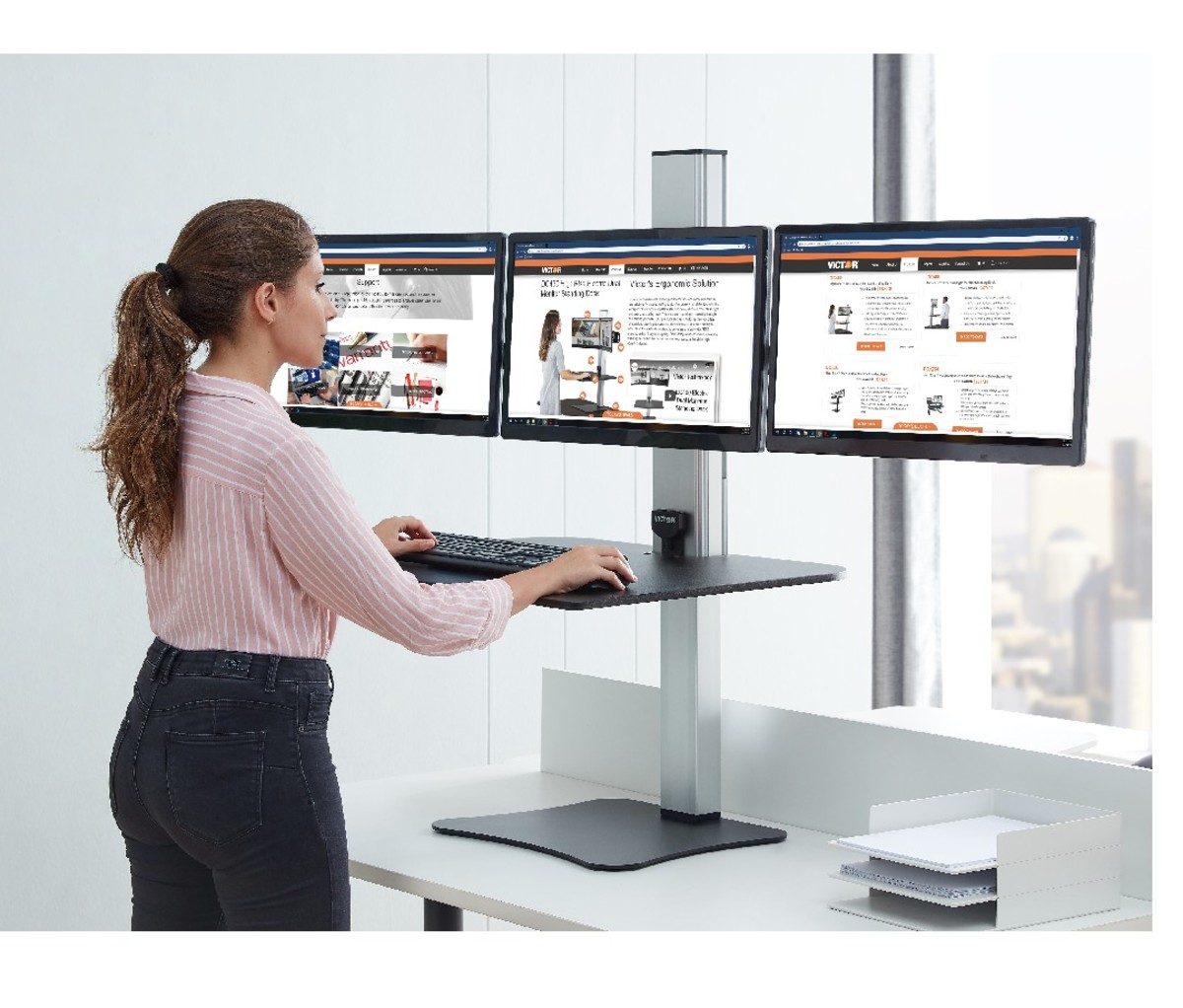 Woman standing at work on a Victor DC475 High Rise Electric Triple Monitor Standing Desk