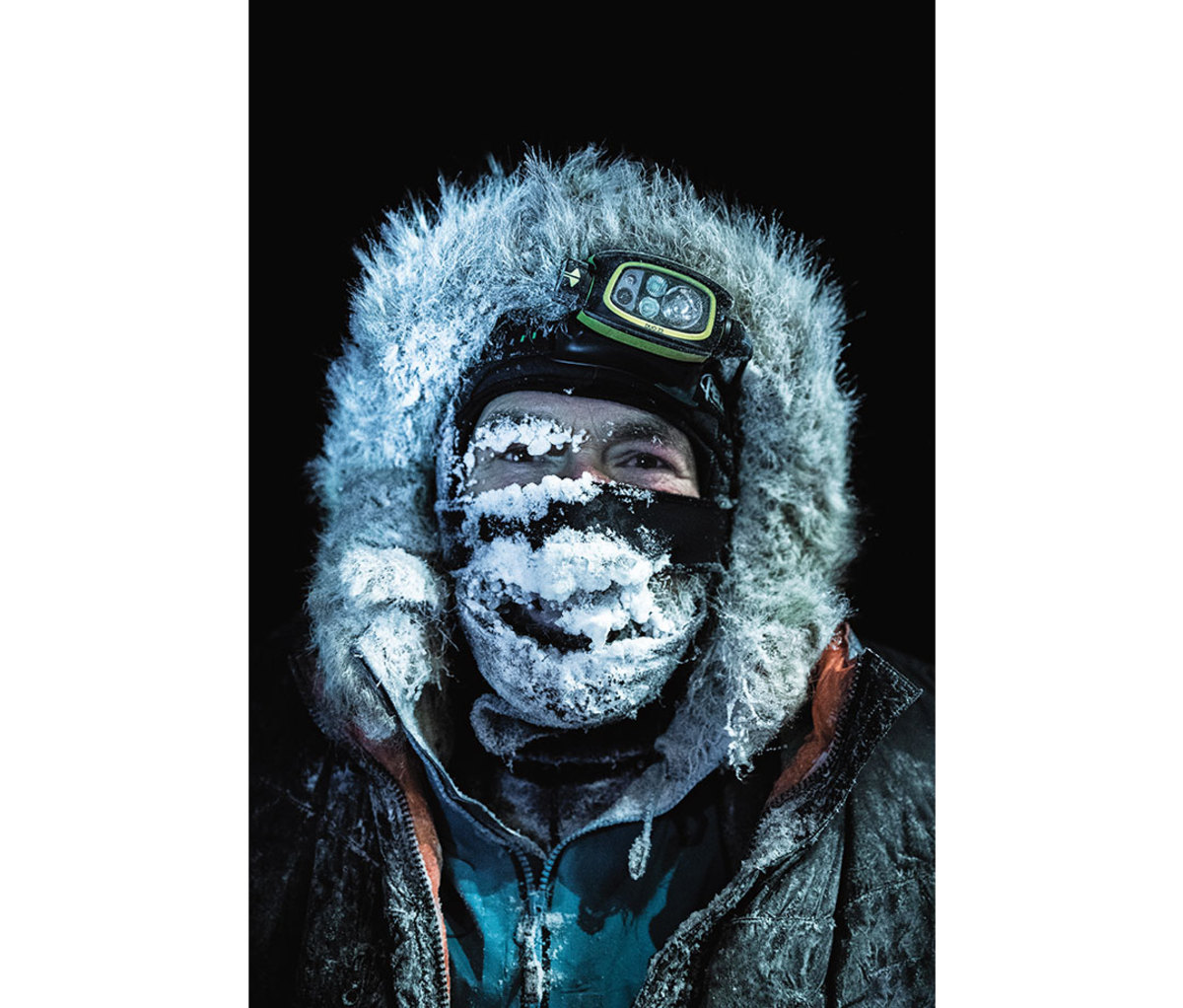 Man wearing fur hood and head lamp with frost covering face