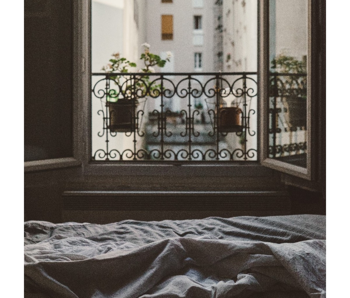 Apartment bedroom with open wrought-iron window overlooking neighboring building