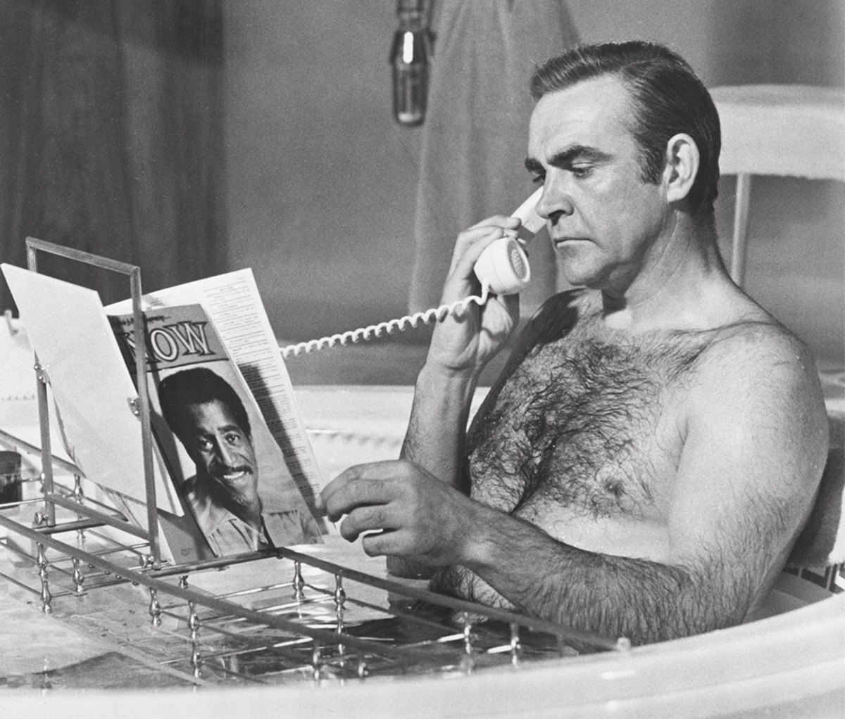 Acteur Sean Connery leest en praat aan de telefoon terwijl hij in bad zit