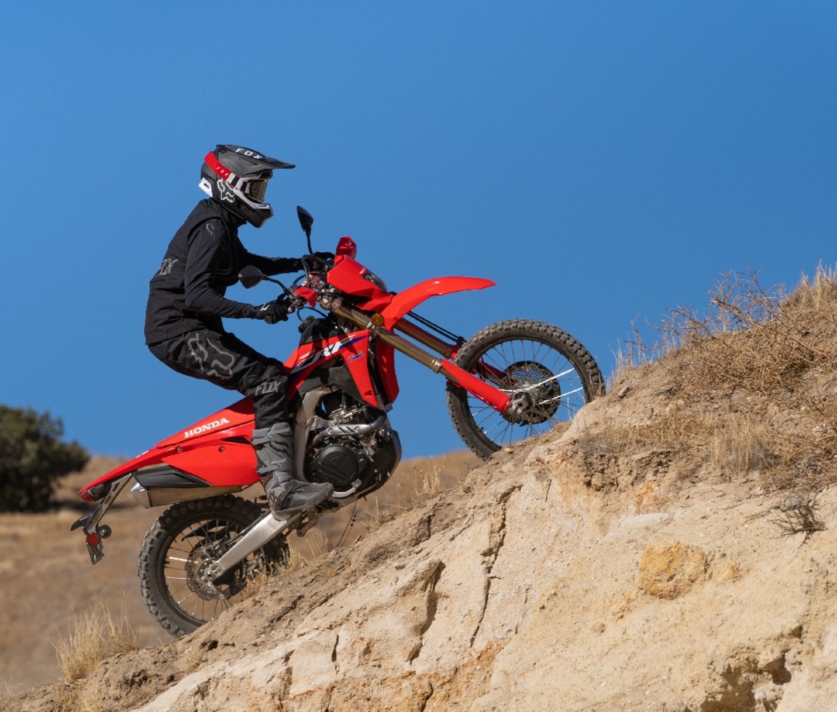 Man riding red dirt bike up steep hill