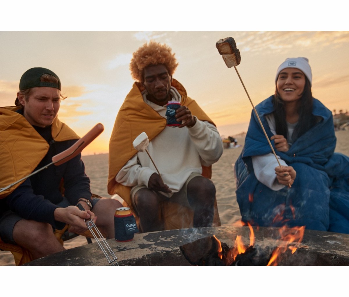 Two men and woman roasting marshmallows on beach bonfire