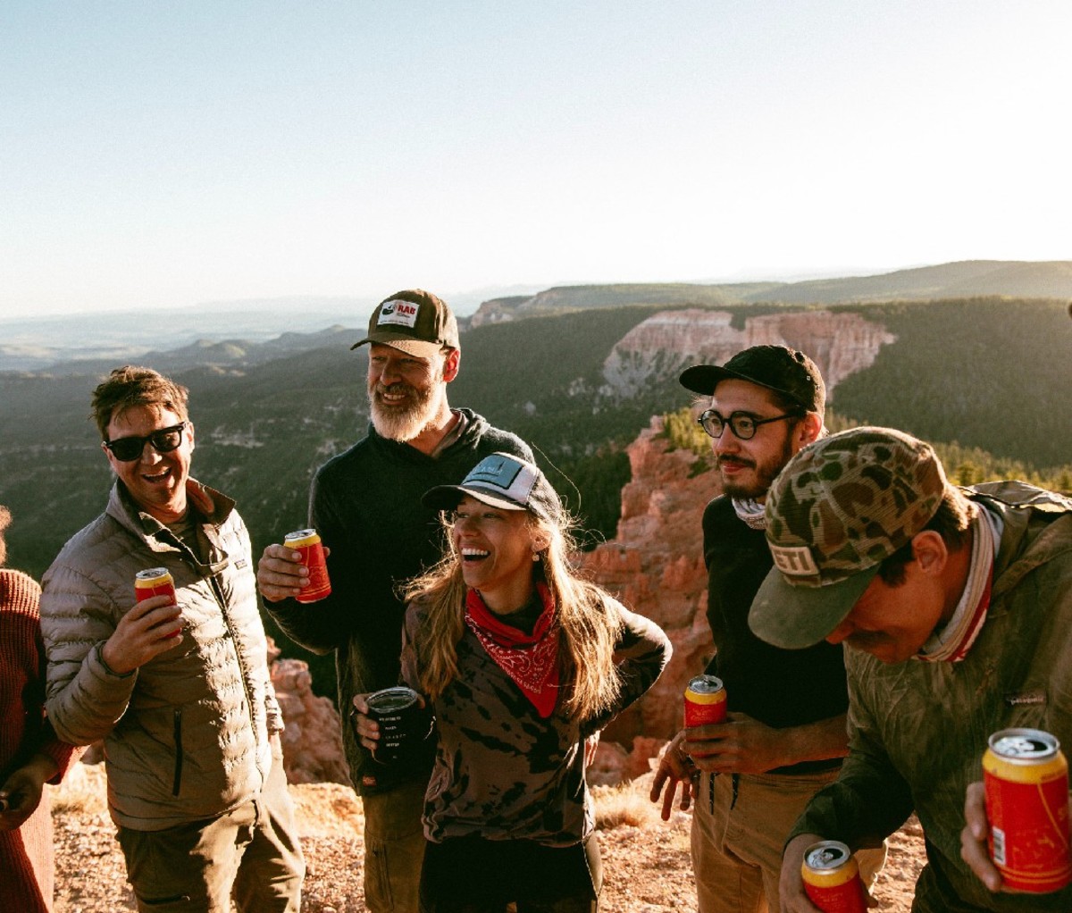 Group of men and women standing at top of ledge drinking beers